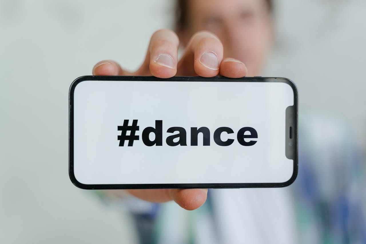 Close-up of a smartphone displaying #dance, held by a young adult.