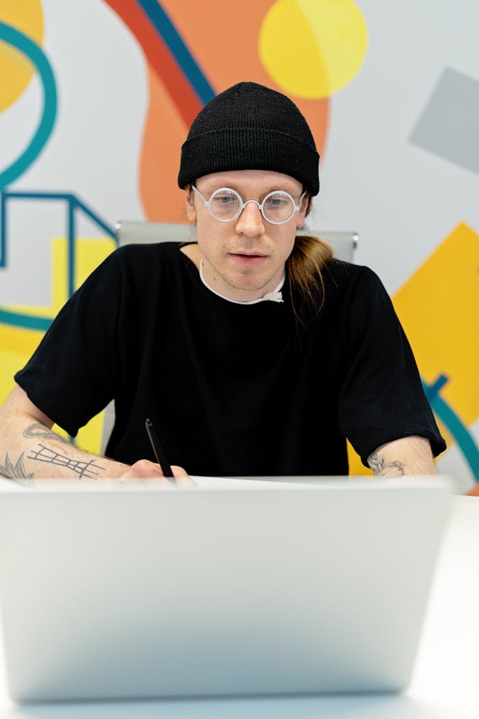 Focused young man in black beanie at laptop, modern workspace.